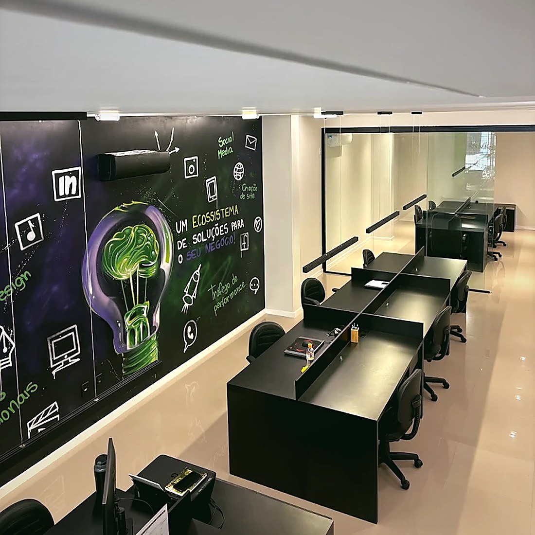 Estações de trabalho do time diante do mural da agência